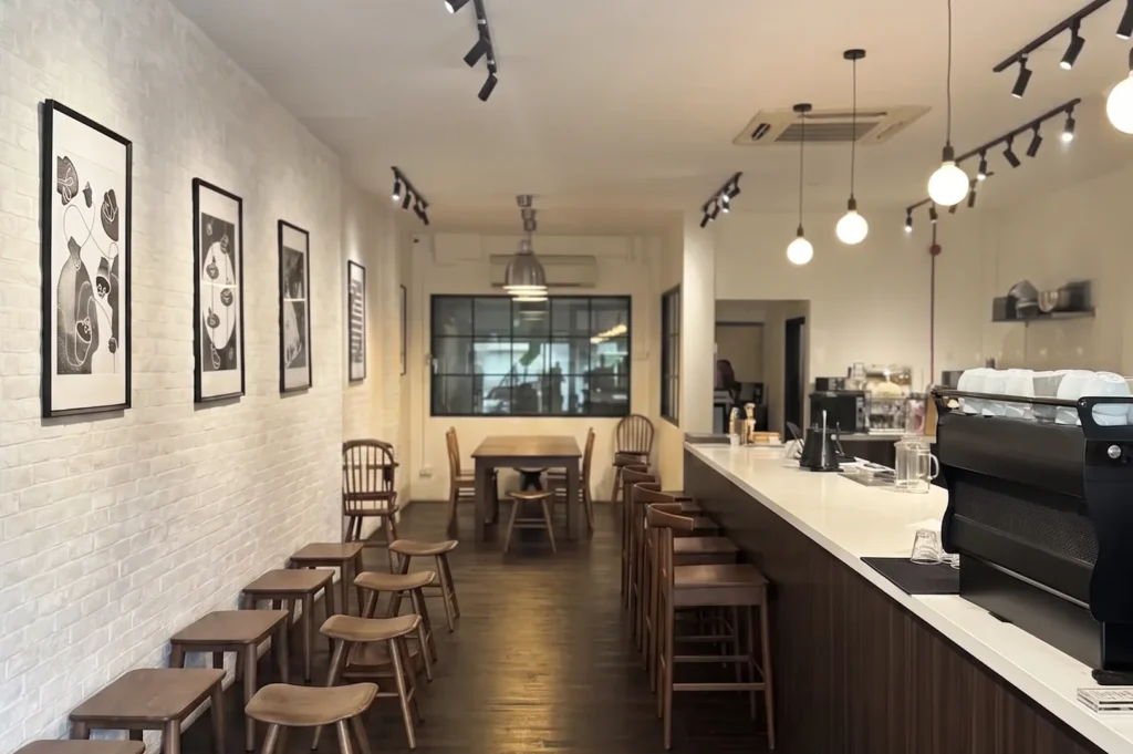Cozy minimalist interior of Pocket by Flip Coffee Roasters featuring wooden stools, white brick walls with framed artwork, and a long espresso bar.