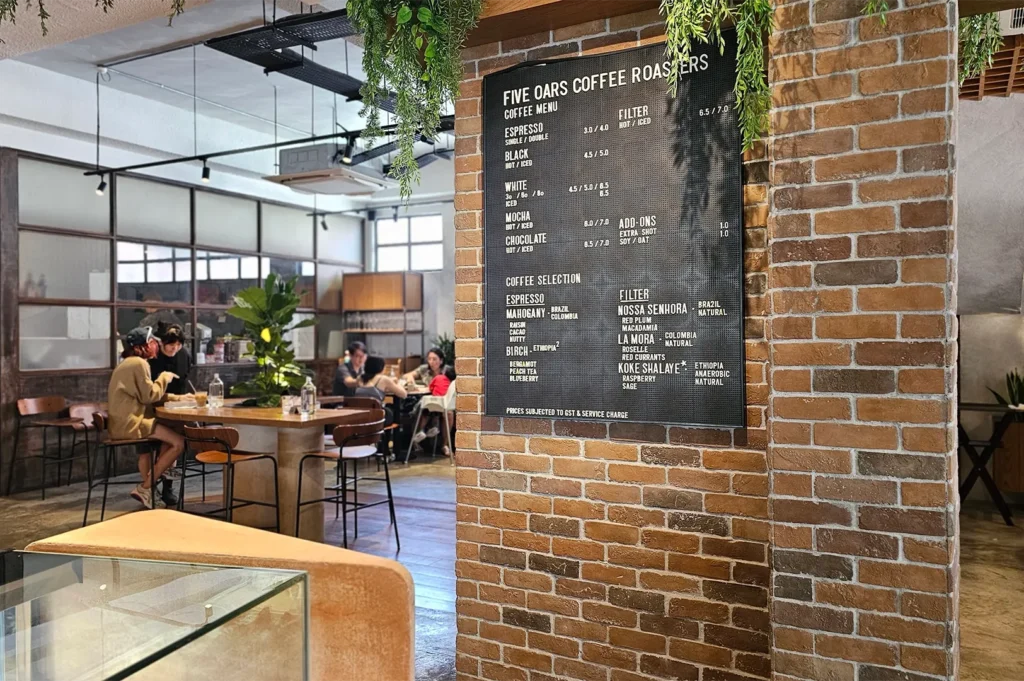 A black letterboard menu displaying coffee selections and blends mounted on a rustic brick pillar inside Five Oars Coffee Roasters cafe.
