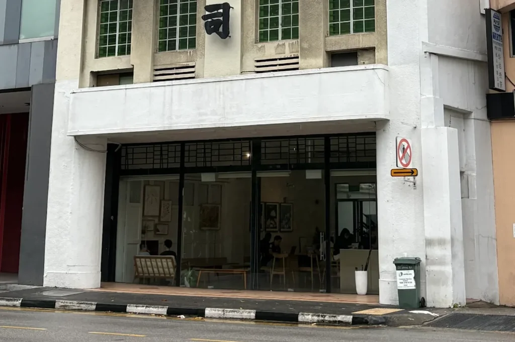 The minimalist glass shopfront facade of Apartment Coffee cafe located in a historic building with traditional Chinese characters on the upper architectural level in Singapore.