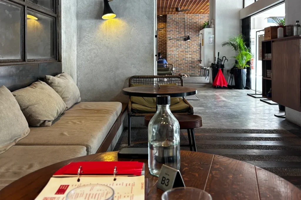 Comfortable indoor lounge seating area at Five Oars Coffee Roasters featuring a long beige fabric sofa with plush pillows and small round wooden tables.