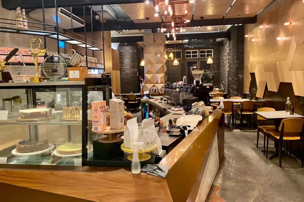 A long sleek wooden espresso bar and glass pastry display case showcasing cakes inside a warmly lit contemporary cafe.