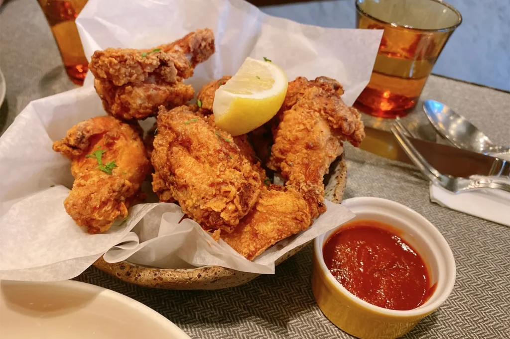 A basket of crispy golden-brown southern fried chicken wings served with a lemon wedge and a side bowl of savory red dipping sauce.