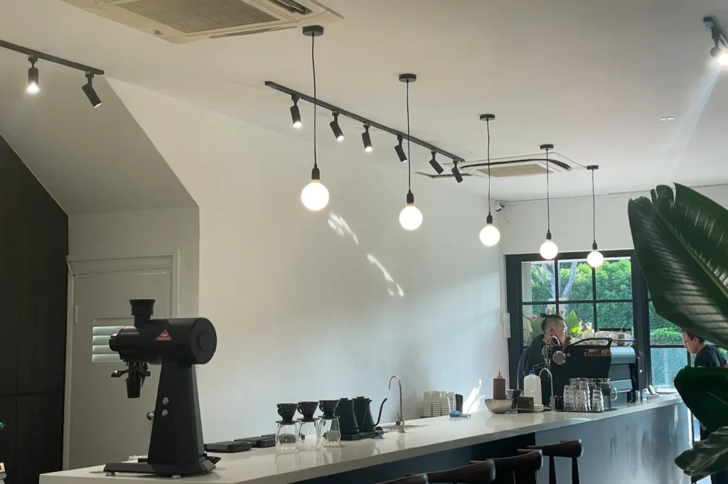 Modern clean minimalist coffee bar counter inside Pocket Coffee Roasters, featuring hanging bulb lights, a professional grinder, and a pour-over setup.