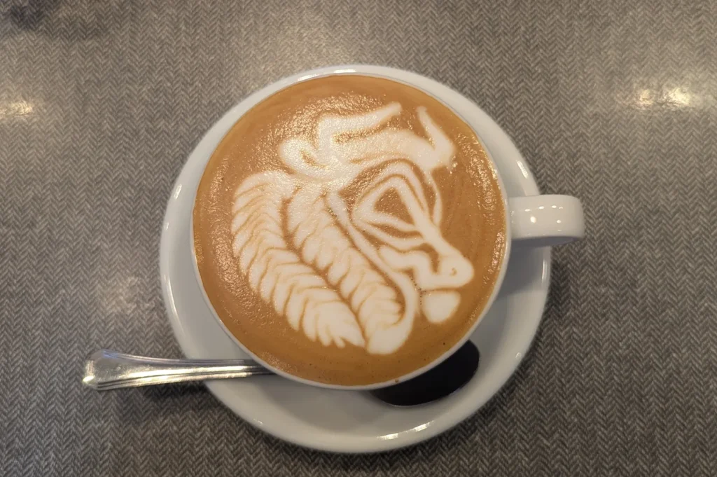 Top-down view of a creamy caffe latte inside a white porcelain cup with highly detailed and artistic foam latte art.