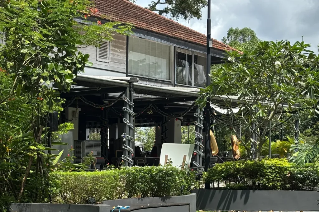 Daytime view of the historic colonial-style building of The Summerhouse restaurant, surrounded by manicured green hedges, trees, and outdoor seating structures.