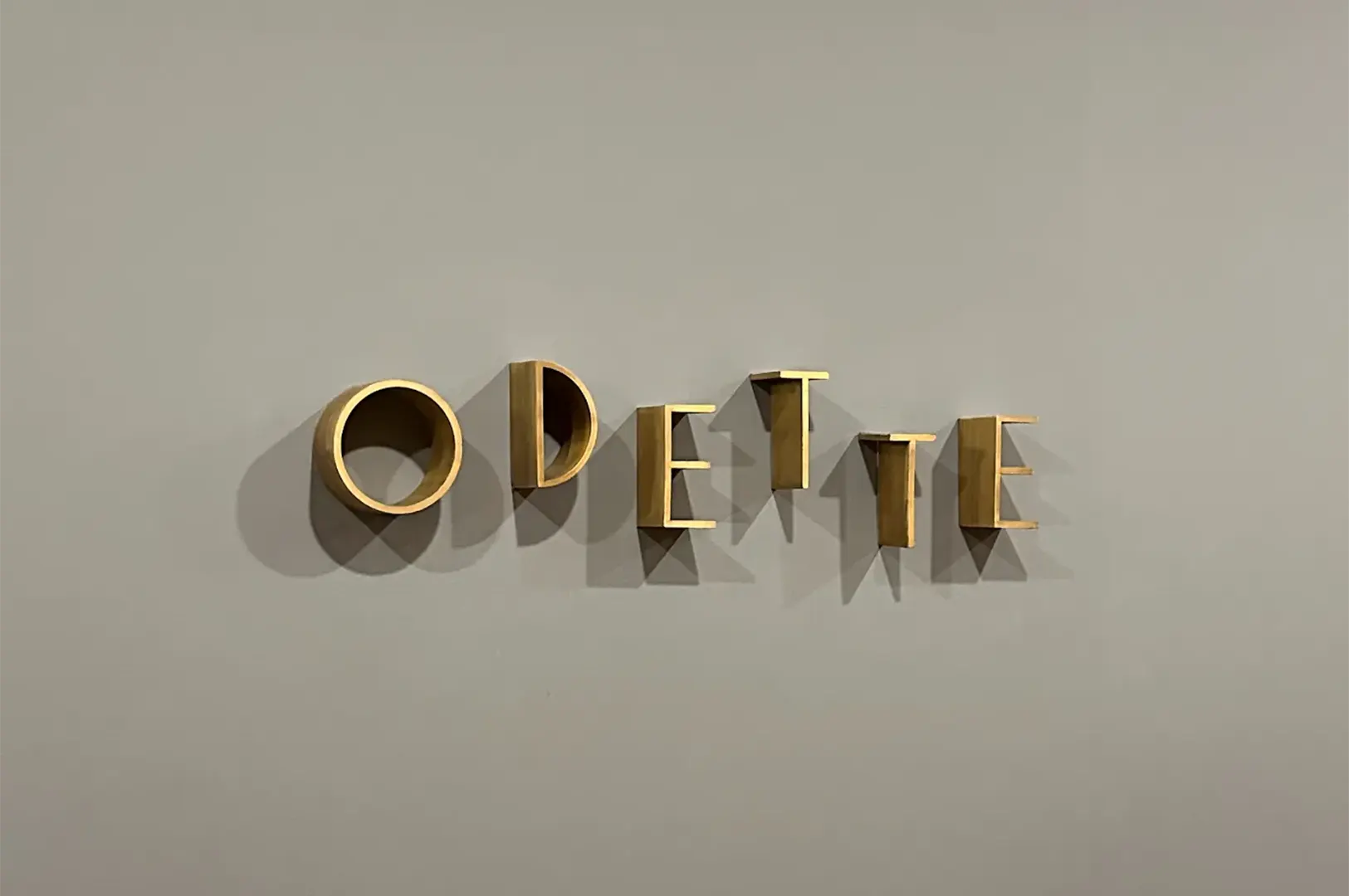 Gold 3D lettering spelling Odette mounted on a minimalist neutral wall at Odette restaurant in Singapore.