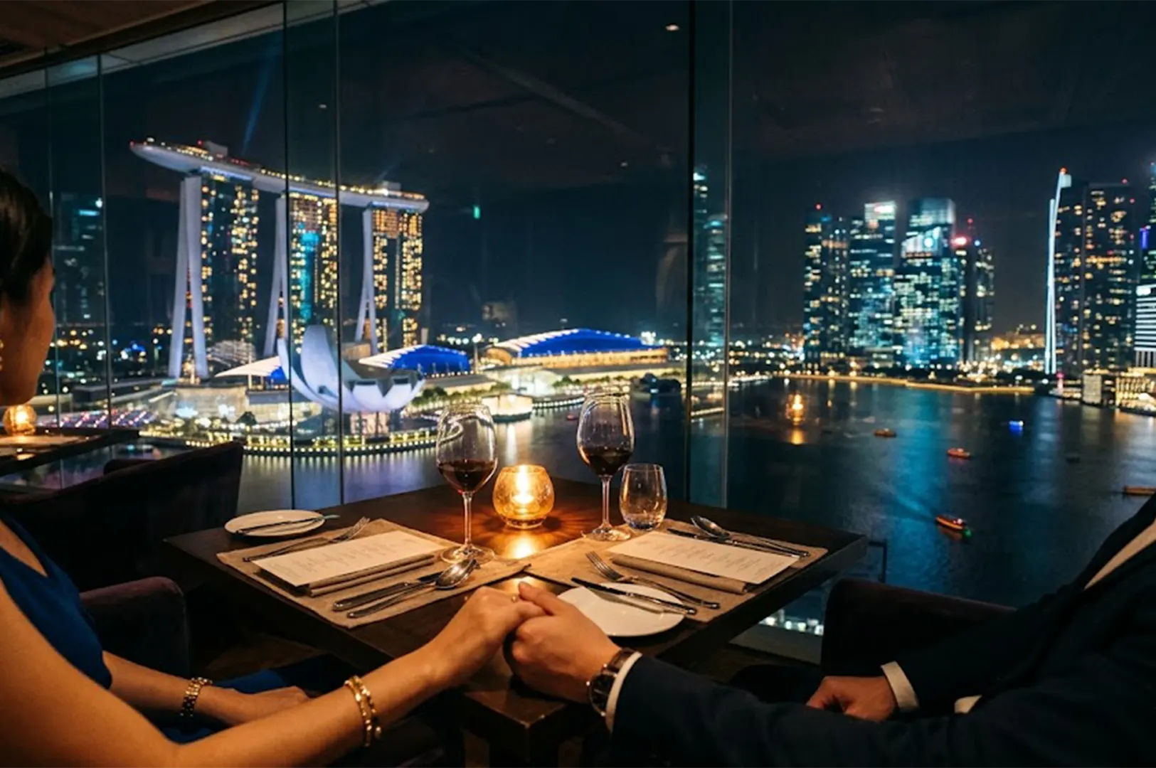 Couple holding hands at a candlelit table during a romantic fine dining date overlooking Marina Bay Sands night skyline in Singapore.