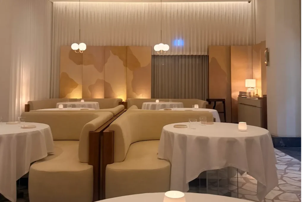Warmly lit luxury dining area at Odette with cream curved booth seating, round tables, and abstract wall art panels.