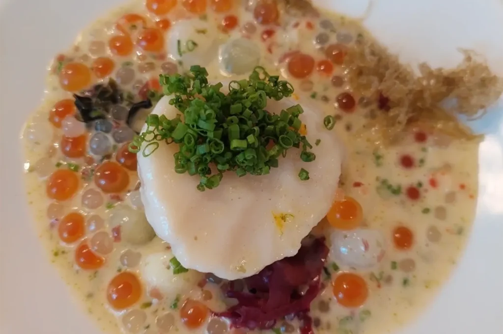 Gourmet French haute cuisine dish featuring a seared scallop, fresh salmon roe caviar, pearls, and microgreens in rich broth at Odette.