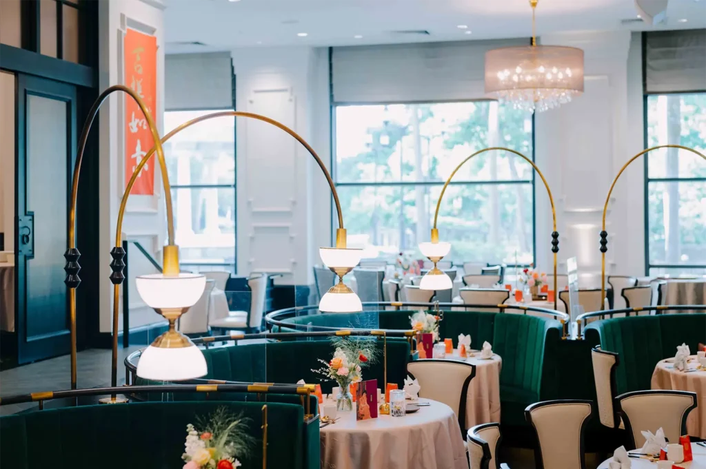 Elegant restaurant seating area featuring curved green velvet booths, arched gold floor lamps, and round dining tables.