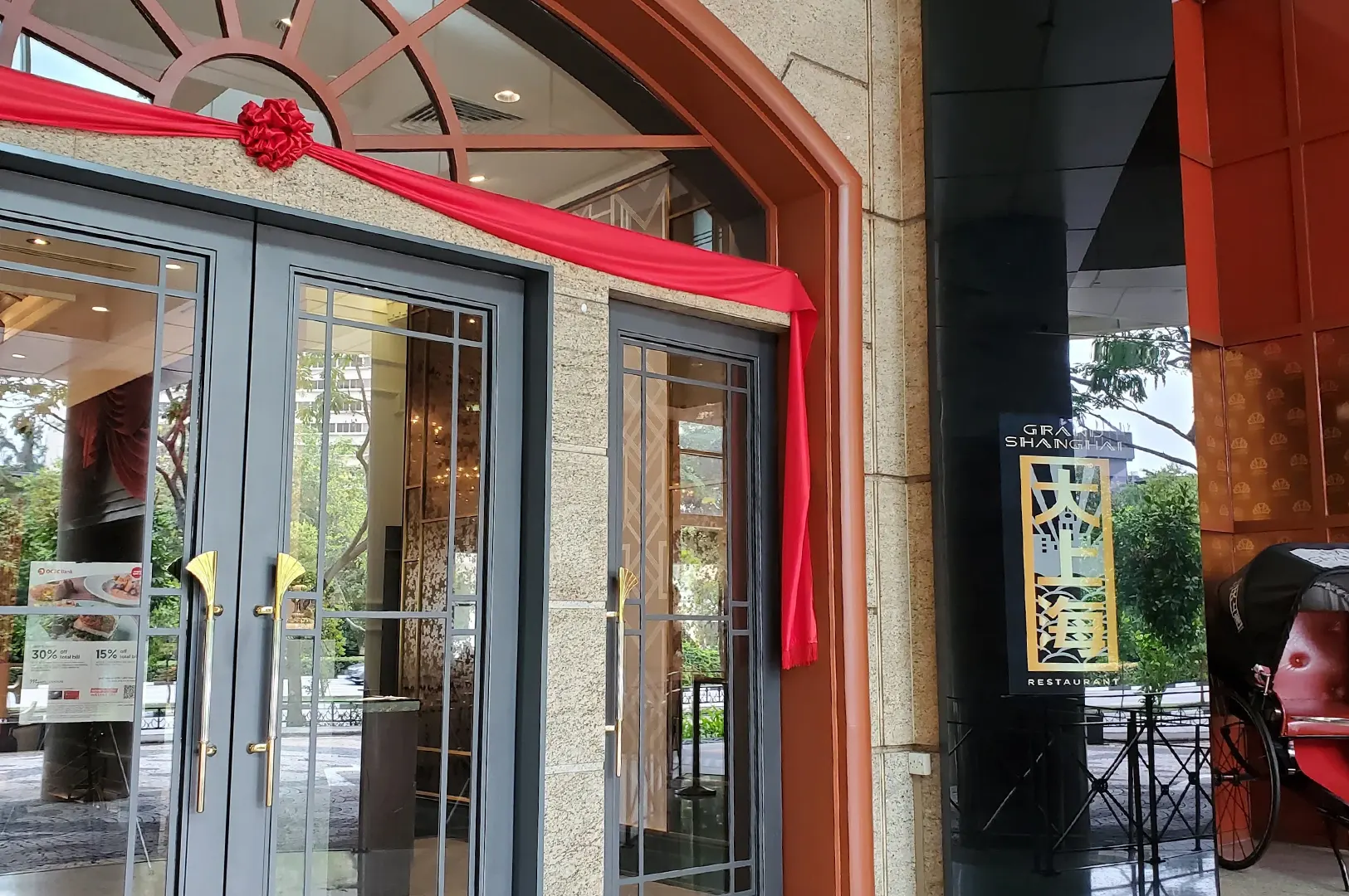Entrance of Grand Shanghai Restaurant featuring glass double doors with red ceremonial ribbon and decorative sign post.