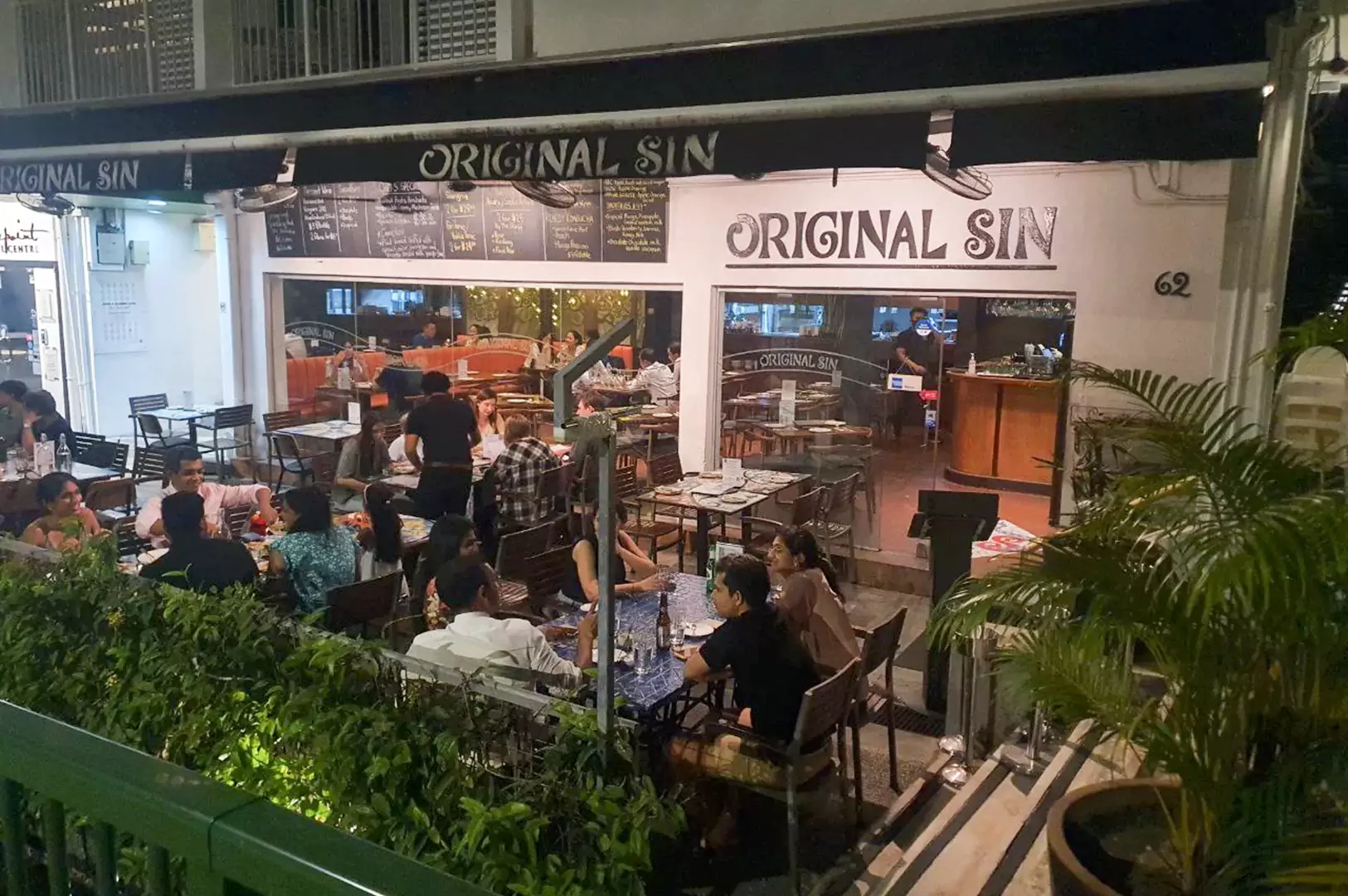 Bustling outdoor dining area and storefront of Original Sin Mediterranean restaurant at night in Holland Village, Singapore.