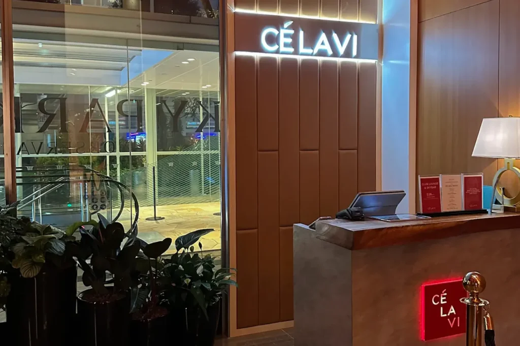 Modern wooden entrance desk with glowing CÉ LA VI logo and indoor plants at Marina Bay Sands.