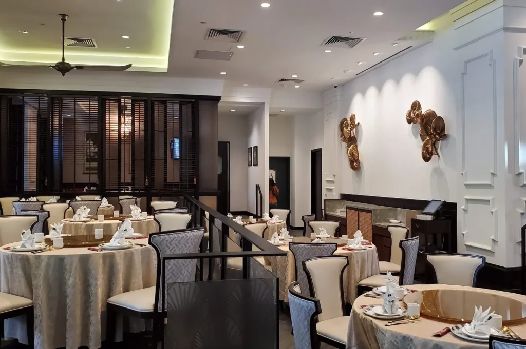 Elegant indoor dining area of Grand Shanghai Restaurant with round tables, ivory tablecloths, patterned chairs, and contemporary wall sculptures.