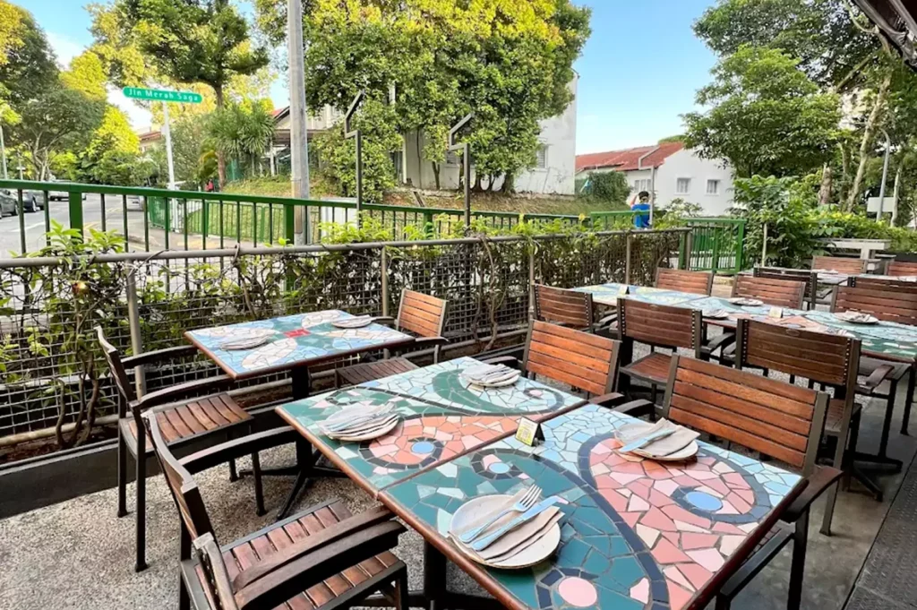 Outdoor terrace dining at Original Sin showing colorful mosaic-tiled tables set for lunch along Jalan Merah Saga.