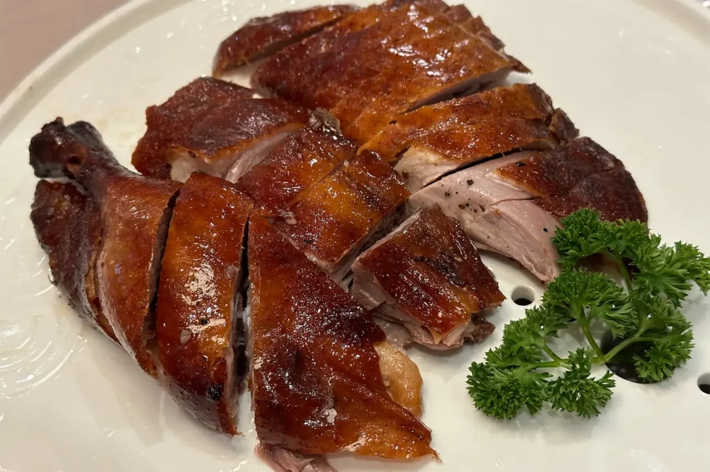 Crispy roasted Peking duck sliced into pieces served on a white plate with fresh parsley garnish.