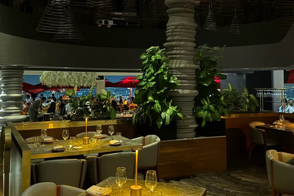 Luxurious indoor restaurant dining room featuring spiral architectural pillars, lush green plants, and warm table lamps.