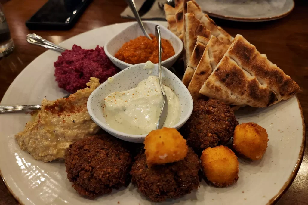 Original Sin Mediterranean mezze platter featuring falafel, fried halloumi bites, pita bread, hummus, beetroot dip, and tzatziki.