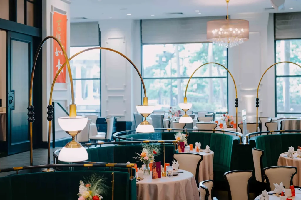 Stylish dining space with deep green velvet curved booth seats, modern arch lamp fixtures, and elegant table arrangements.