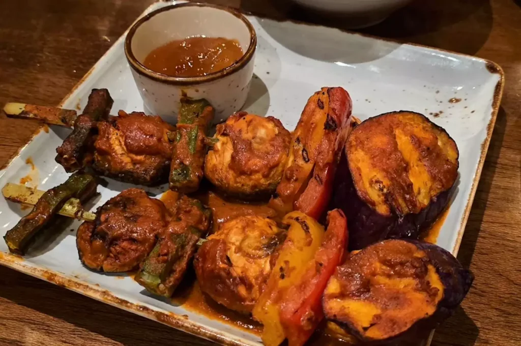 Platter of grilled Mediterranean vegetable skewers with zucchini, mushrooms, bell peppers, and roasted eggplant served with dipping sauce at Original Sin.
