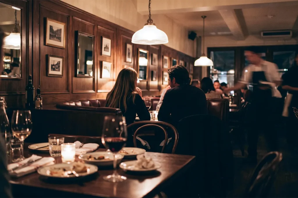 A couple enjoying an intimate dinner conversation in a cozy, dimly lit restaurant with wood paneling.
