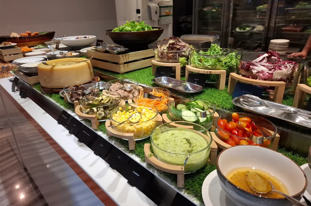 Fresh salad bar counter featuring a large wheel of cheese, mixed greens, cherry tomatoes, and dressings at Shangri-La Singapore.