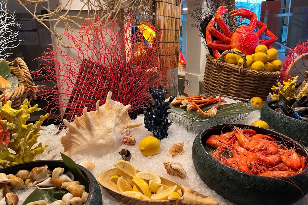Fresh seafood buffet display on ice featuring cooked prawns, crab, mussels, and seashells at Shangri-La Singapore.
